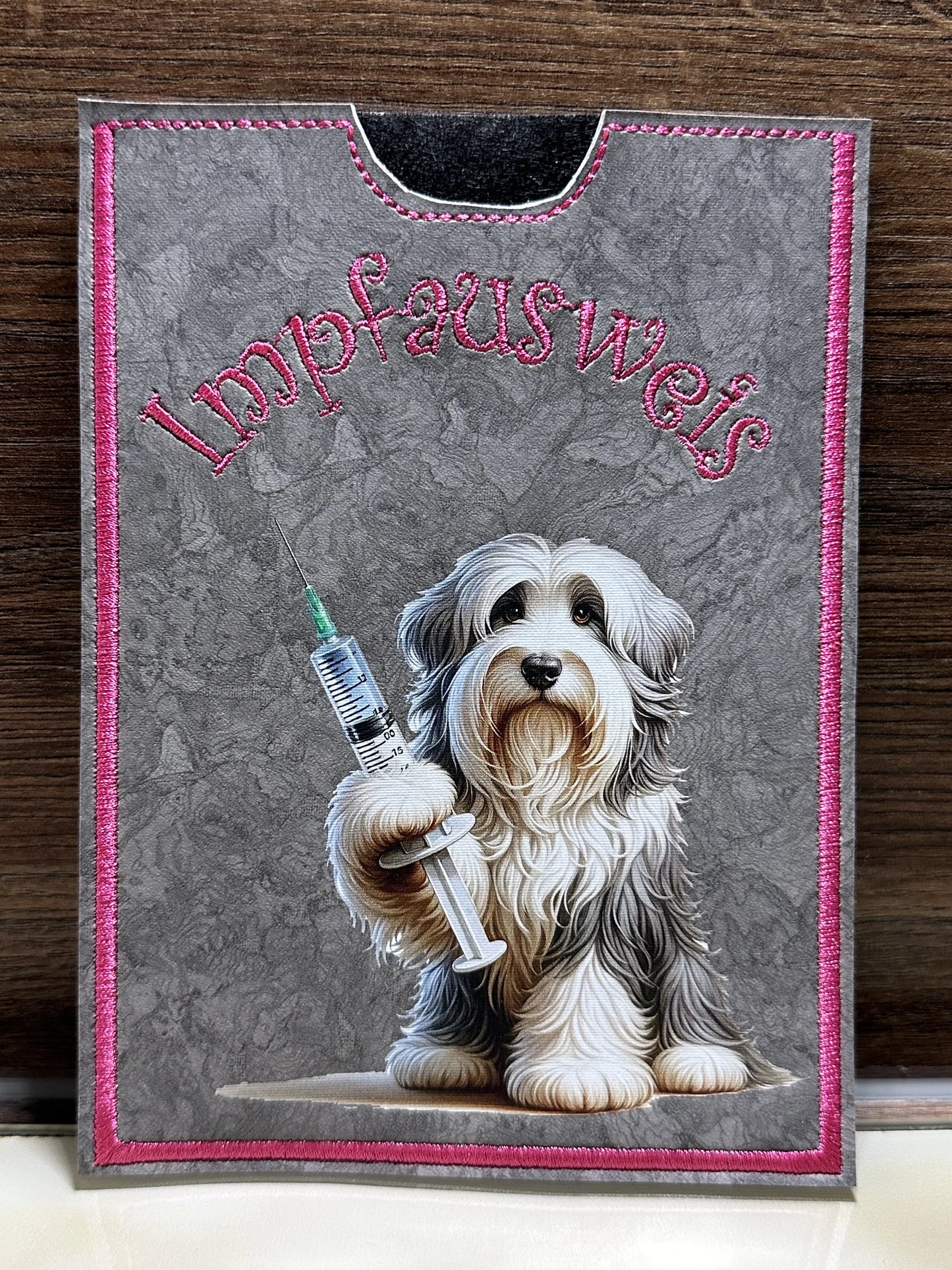 Handgemachte Impfpasshülle 12,5 × 17 cm aus grauem Kunstleder mit pinker Naht und Bearded Collie Motiv mit Spritze – passend für EU-Heimtierausweis