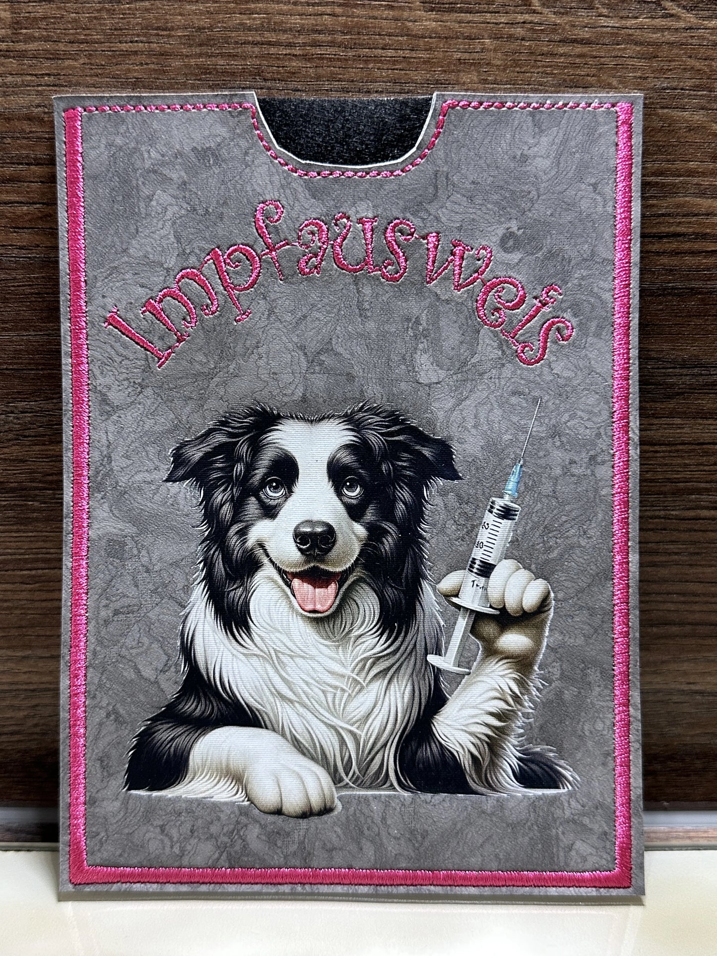 Handgemachte Impfpasshülle 12,5 × 17 cm aus grauem Kunstleder mit pinker Naht und Border Collie Motiv mit Spritze – passend für EU-Heimtierausweis