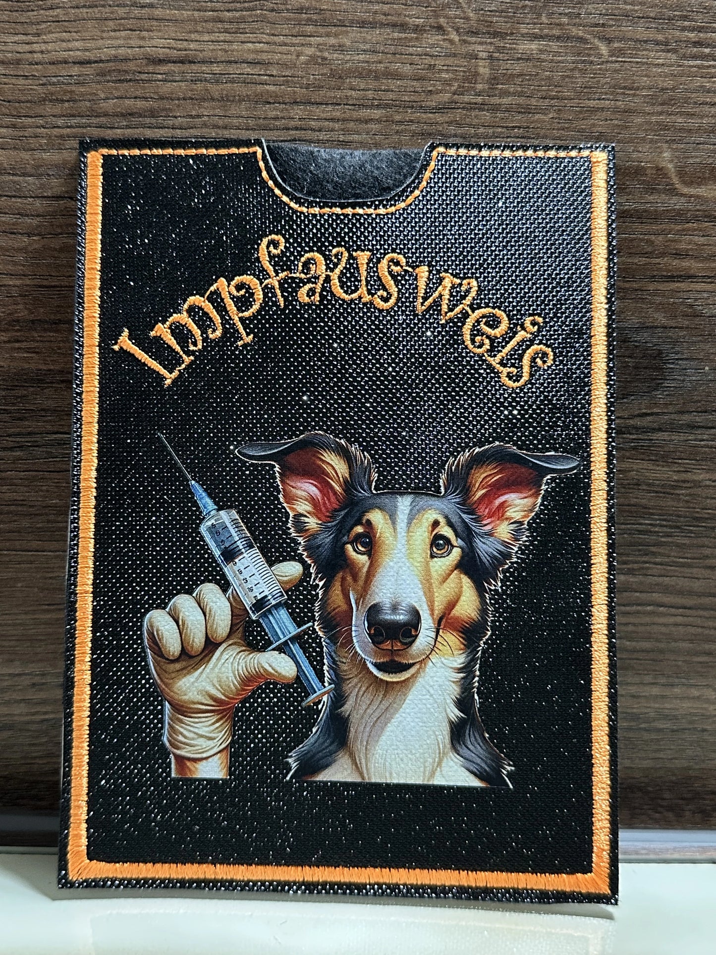 Impfpasshülle Kurzhaar Collie – Vorderseite mit Collie Motiv und Spritze, schwarze Kunstlederhülle mit oranger Naht